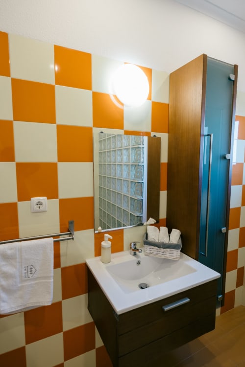 Modern bathroom with orange and cream checkered tiles, white sink, mirror, and dark wood vanity at Figueira House villa in