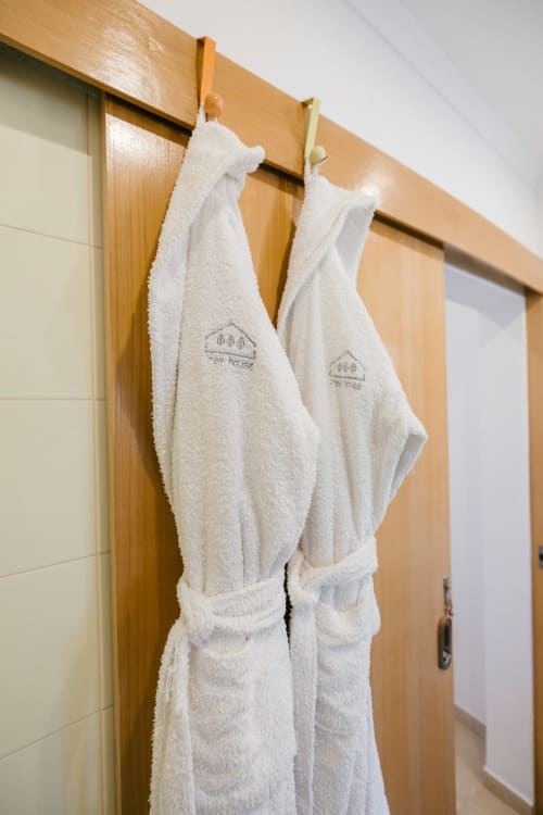 Two white bathrobes with Tree House logo hanging on wooden rod in bathroom at Figueira House villa