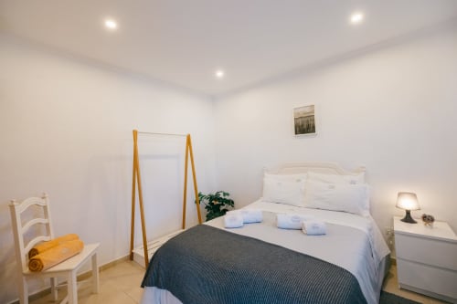 Bright bedroom at Tree House villa in Sesimbra with queen bed, white linens, dark throw, bedside lamp, wooden mirror, potted