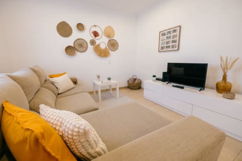 Modern living room at Casa Laranjeira villa with beige sofa, flat-screen TV, woven wall art, and yellow accents in Sesimbra,
