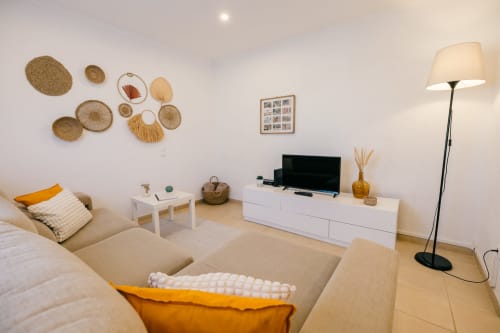 Modern living room at Casa Laranjeira villa in Sesimbra with beige sofa, flat-screen TV, white furniture, and natural décor