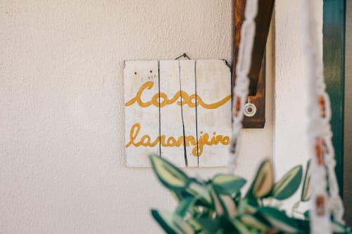 Wooden sign reading 'Casa Laranjeira' in yellow script at Tree House villa in Sesimbra, Portugal, with green plant foliage