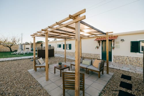 Wooden pergola with outdoor seating at Casa Laranjeira villa in Sesimbra, Portugal, with lounge chairs and dining area