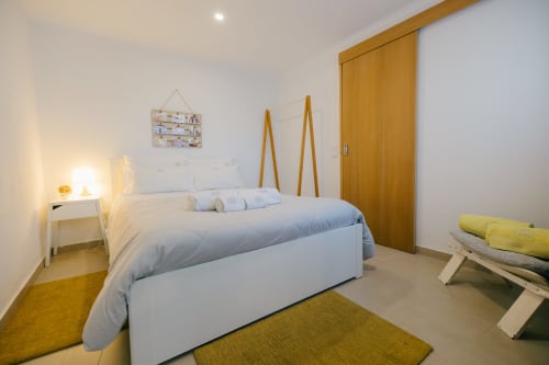 Modern bedroom at Tree House villa Limoeiro House in Sesimbra with bed, wooden accents, yellow rugs, and white nightstand