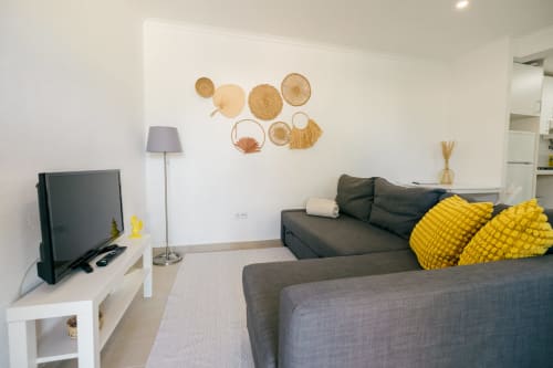 Modern villa living room with grey sofas, yellow pillows, TV, floor lamp, and woven wall décor at Tree House in Sesimbra
