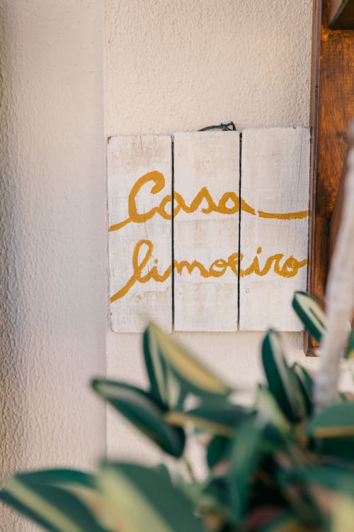 Rustic white wooden sign reading 'Casa Limoeiro' with golden text at Tree House villa in Sesimbra, Portugal, with blurred