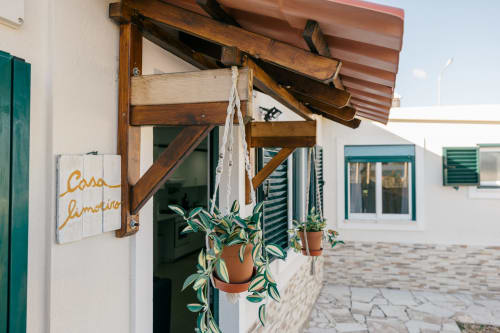 Casa Limoeiro villa entrance with wooden awning, hanging potted plants, and green shutters at Tree House Sesimbra