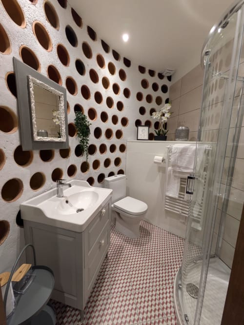 Modern bathroom at Manoir Saint Joseph with decorative circular wall pattern, white vanity, toilet, and walk-in shower