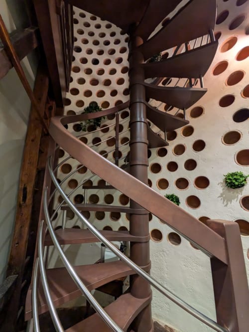 Spiral staircase with metal handrail in Manoir Saint Joseph's Dovecote bedroom, featuring perforated wall details and potted