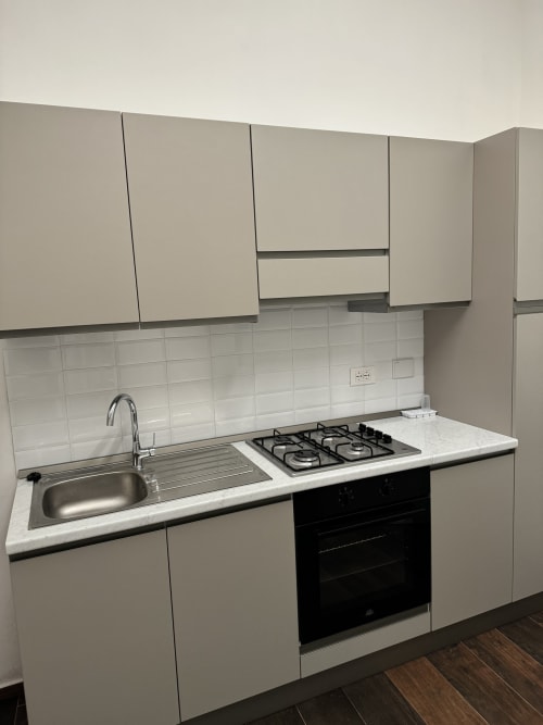 Cucina moderna con mobili bianchi, piano cottura a gas, lavello e rivestimento in piastrelle bianche nell'appartamento Enjoy House Bracciano,