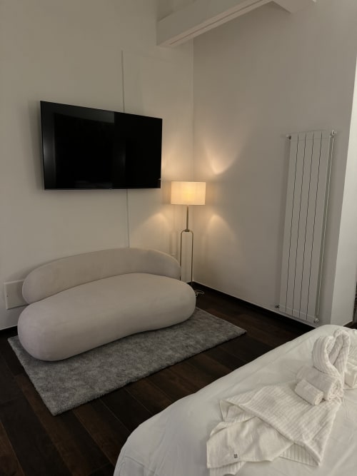 Camera moderna all'Enjoy House Bracciano con divano curvo, TV a parete, lampada e termosifone in stile minimalista