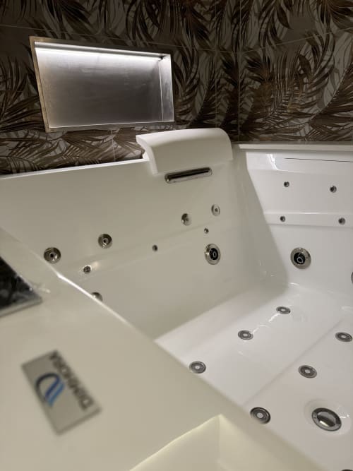 Esclusiva vasca idromassaggio bianca con getti d'acqua presso l'appartamento Enjoy House Bracciano, con sfondo di carta da parati decorativa con piante