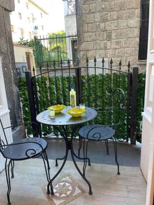 Affascinante terrazza al San Nicola Suite di Sorrento con arredamenti in ferro battuto, ciotole gialle e ringhiere ricoperte di edera