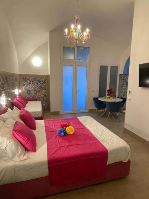 Camera moderna di San Nicola Suite a Sorrento con biancheria rosa, lampadario colorato e vista sulla città