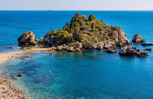 Isola rocciosa con vegetazione rigogliosa nelle acque turchesi cristalline vicino a Taormina, Sicilia