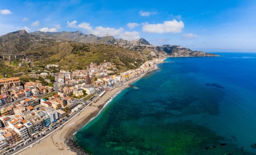 Vista aerea degli Appartamenti ToviMar a Taormina con il turchese Mar Mediterraneo e spiaggia sabbiosa