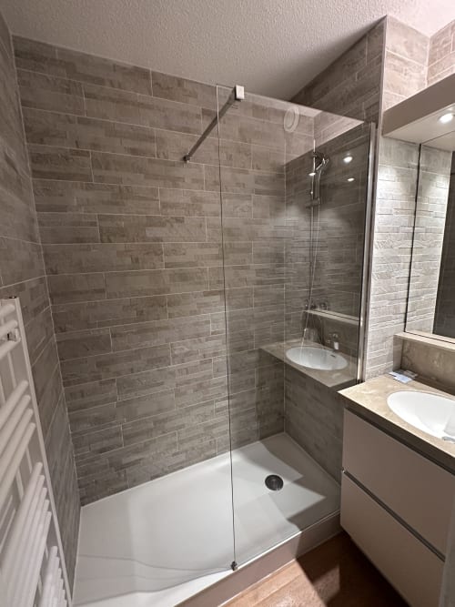 Salle de bain moderne avec douche carrelée grise, double vasque et sèche-serviettes chauffant à l'Hôtel Studios La Rochetaillée