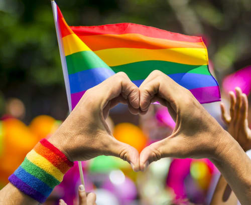 Geste de cœur avec drapeau arc-en-ciel lors d'une célébration LGBTQ, symbolisant l'amour et l'inclusion