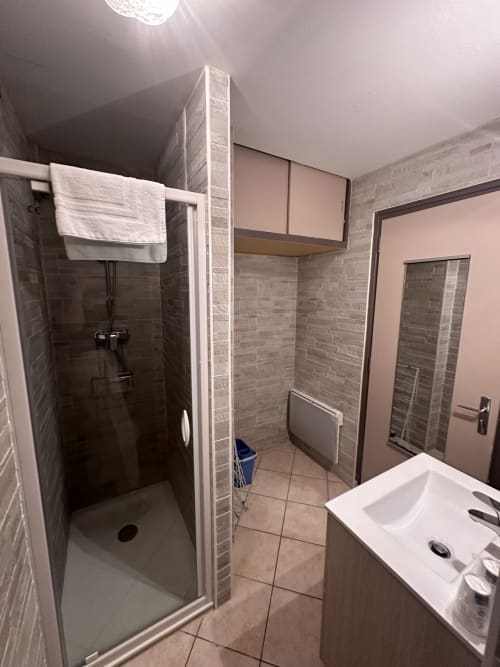 Salle de bains moderne avec douche à l'italienne, lavabo blanc et carrelage gris à l'Hôtel Studios La Rochetaillée