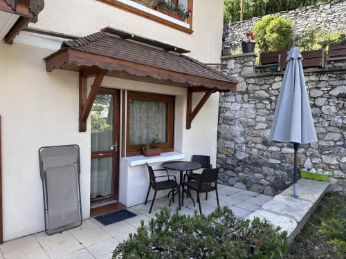 Patio de l'appartement du Hôtel Studios La Rochetaillée avec table de repas, parasol et mur en pierre à Brides-les-Bains