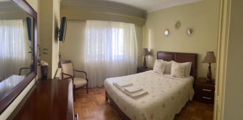 Quarto luminoso na Casa Da Avó Ilda em Matosinhos com cama queen, móveis em madeira escura, paredes amarelas e vista para o oceano