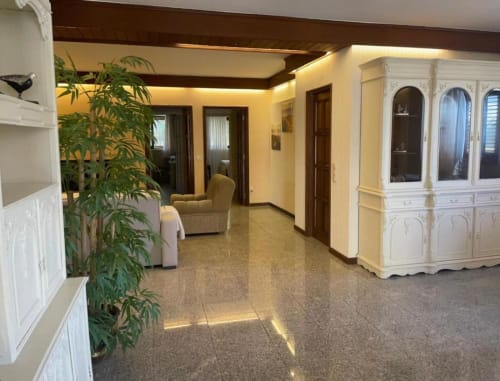 Espaçosa sala de estar na Casa Da Avó Ilda com paredes cor creme, pisos azulejos, planta verde, móvel branco e múltiplas aberturas