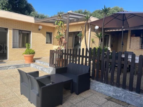 Pátio da Casa Da Avó Ilda com espreguiçadeiras pretas, pérgola, guarda-sol e vista para o jardim em Matosinhos