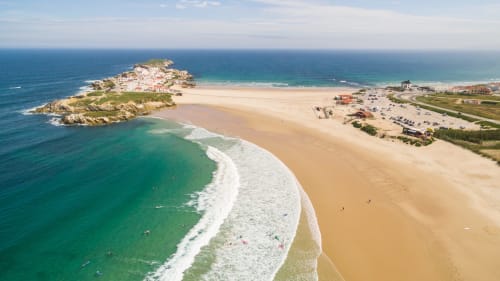 Aerial view of Bombarral beach with turquoise waves, golden sand, and coastal village near Óbidos, Portugal