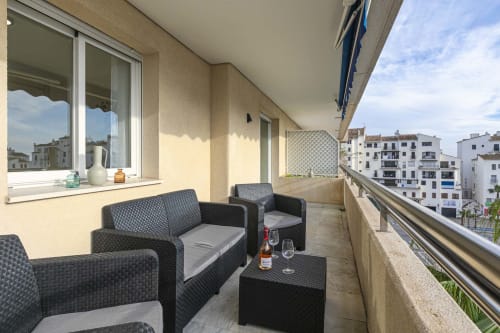 Spacious balcony at Marbella Home Rentals apartment with rattan seating, city views of Puerto Banús, and modern amenities
