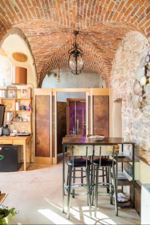 Sala benessere CasaRosada a Vidracco con soffitto in mattoni ad arco, zona pranzo, cucina e muri in pietra rustica