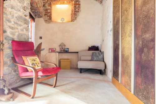 Accogliente sala wellness di CasaRosada B&B a Vidracco con poltrona rossa, divano e muri in pietra a vista