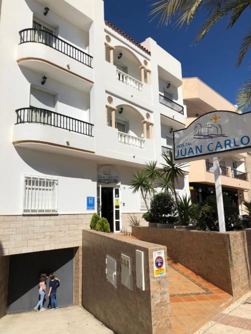 Hostal Juan Carlos en Carboneras, España: fachada blanca con balcones, palmeras y patio de entrada