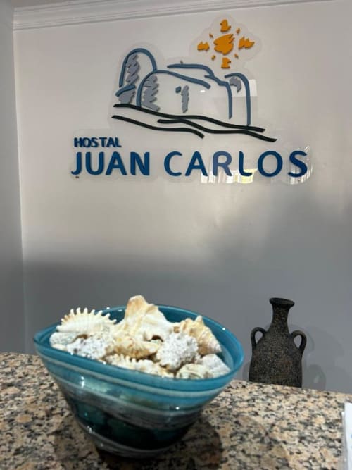 Letrero de entrada del Hostal Juan Carlos con cuenco turquesa de pan en la barra, Carboneras