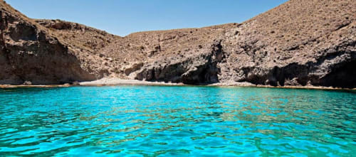 Cala turquesa con playa de arena rodeada de acantilados rocosos cerca de Carboneras, España