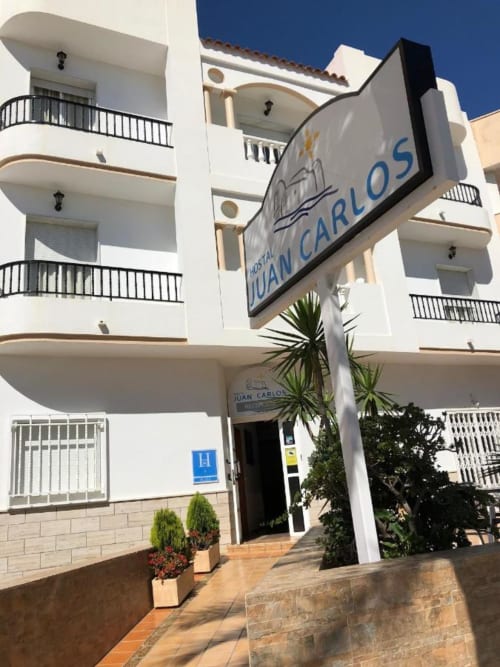Fachada exterior del Hostal Juan Carlos en Carboneras, edificio blanco de varios pisos con señalética direccional