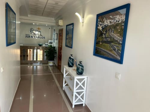 Pasillo de entrada del Hostal Juan Carlos en Carboneras con mostrador de recepción, fotografías costeras enmarcadas y decoración moderna