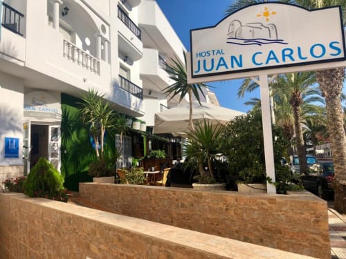 Entrada del Hostal Juan Carlos con edificio blanco, palmeras y señalización acogedora en Carboneras