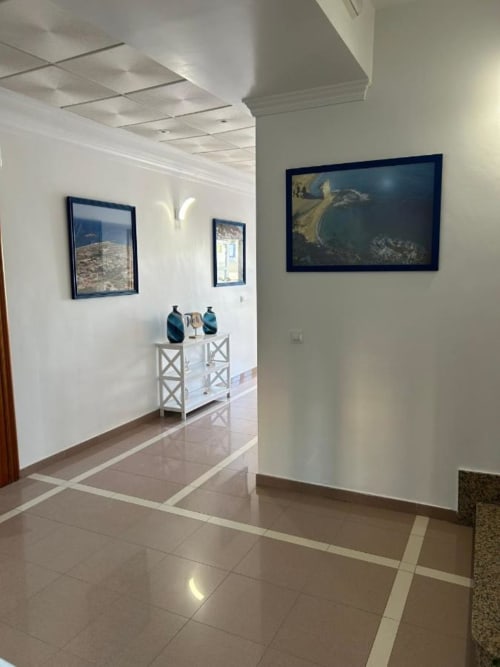 Pasillo moderno del Hostal Juan Carlos en Carboneras con arte costero enmarcado, mueble blanco y pisos de azulejo pulido
