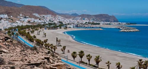 Playa de Carboneras con palmeras, edificios blancos en la ladera y Mar Mediterráneo azul, cerca del Hostal Juan Carlos