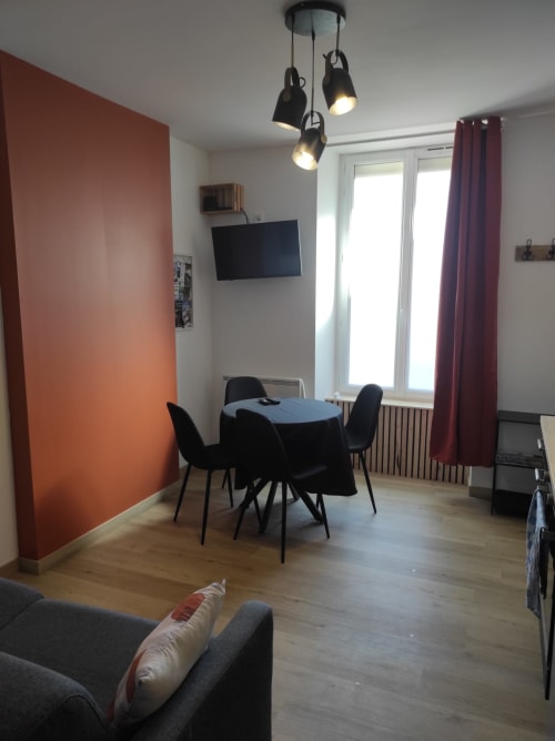 Séjour moderne à l'hôtel Accolade à Châteaudun avec table à manger, chaises noires et mur d'accent orange