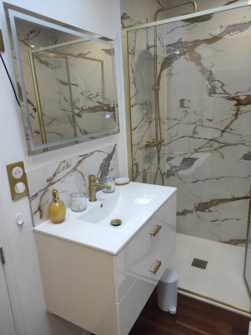 Salle de bain moderne à l'appartement Accolade à Châteaudun : carrelage imitation marbre, vasque blanche, robinetterie laiton et douche vitrée