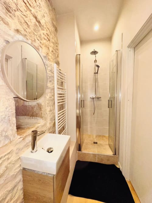 Salle de bain moderne à Vue Sur Gindou avec douche à l'italienne, lavabo blanc, miroir rond et murs en pierre à Gindou, France