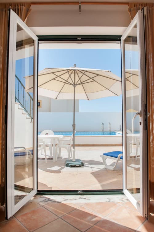 Open French doors revealing beachfront terrace with umbrella, lounge chairs, and ocean view at Home Alliance BnB, Óbidos