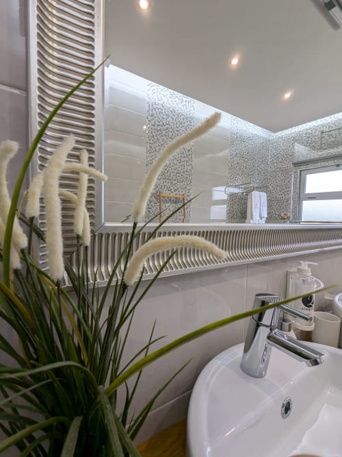 Casa de banho moderna com lavatório branco, radiador, azulejos em mosaico, espelho e planta decorativa na Home Alliance Bombarral