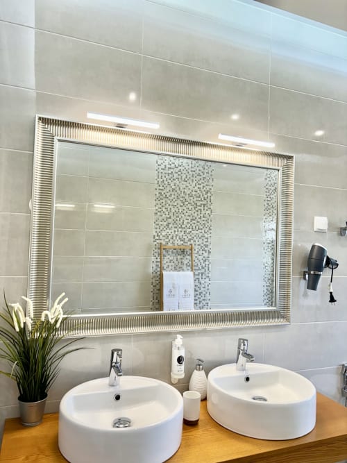 Banheiro moderno do hotel Home Alliance com pias redondas duplas, espelho iluminado e detalhes em azulejos mosaico