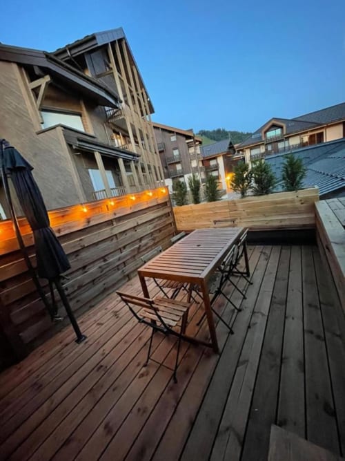 Terrasse en bois avec espace de détente à Duplex les Myrtilles Les Carroz, vue sur les montagnes et bâtiments modernes au crépuscule.