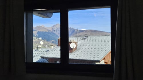 Vue montagnarde depuis la fenêtre de l'appartement de L'écrin des sapins à Aime-la-Plagne, avec pics alpins et bâtiments couverts