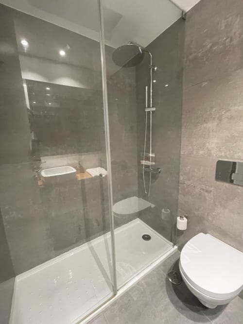 Banheiro moderno nas Casas de Juromenha com chuveiro aberto, vaso sanitário branco, pia e paredes revestidas de azulejos