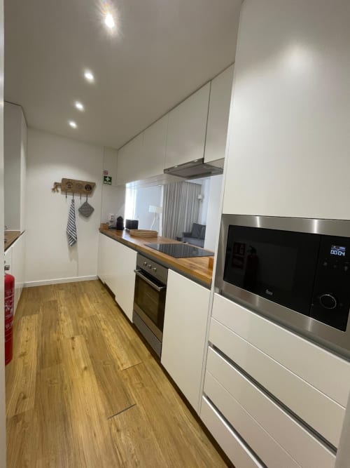 Modern galley kitchen with white cabinetry, wood countertop, stainless steel appliances at Casas de Juromenha