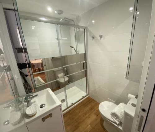 Modern bathroom with glass shower enclosure, white tiles, wooden flooring, and sink at Le 58 Bayeux apartment in Bayeux